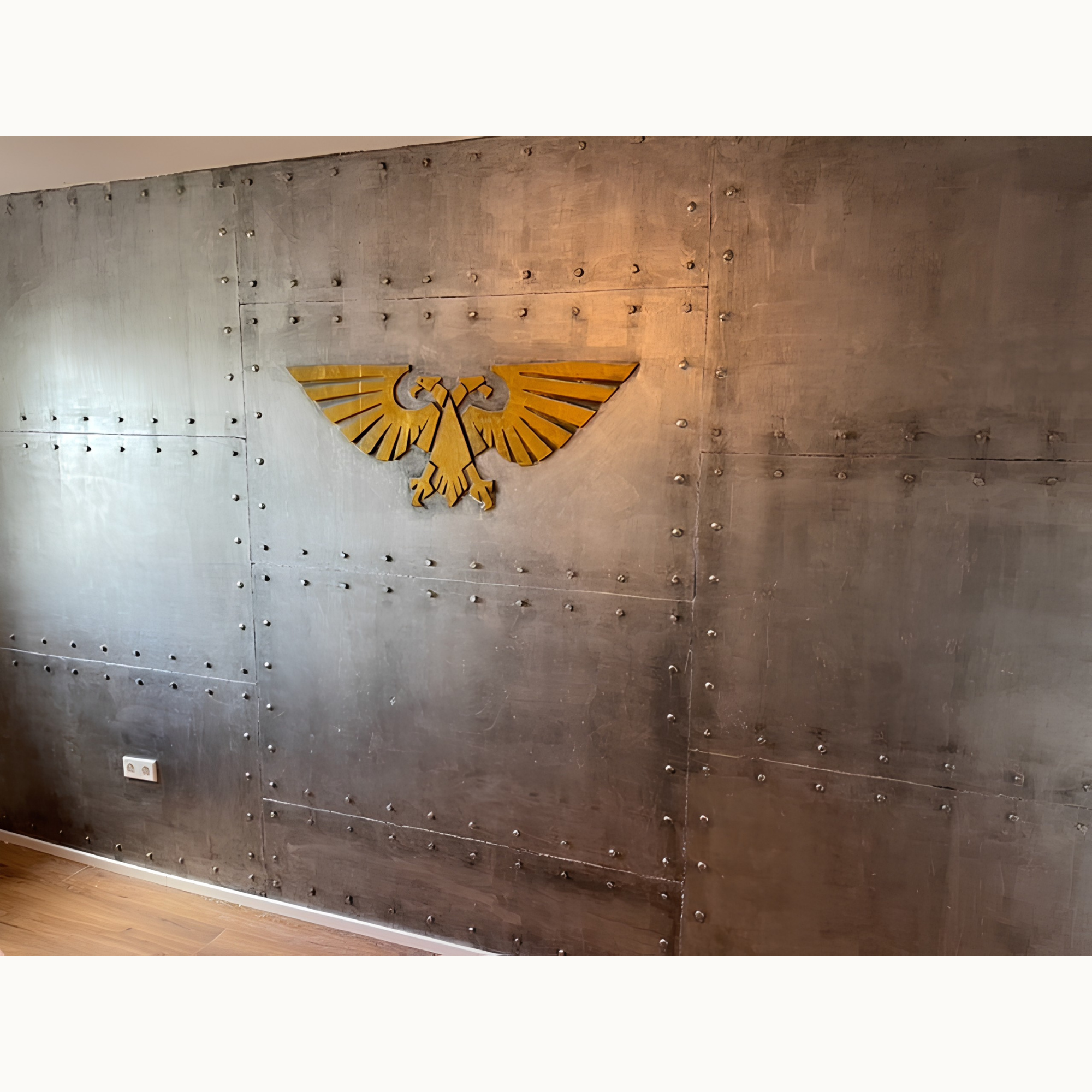 Graue, genietete Metallwand im Industrie-Look mit goldenem Adler-Emblem als Blickfang