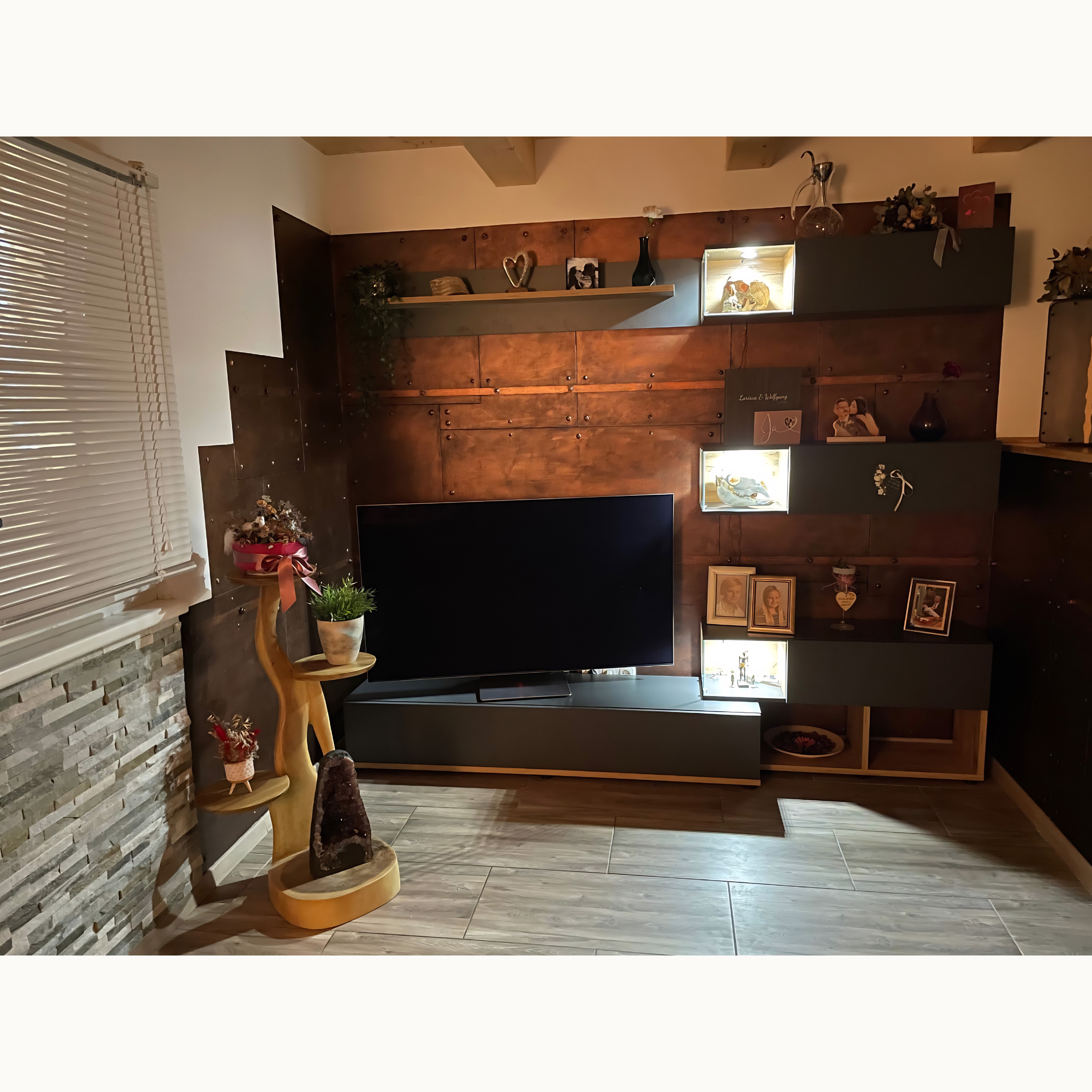 Wohnwand mit Fernseher und Kupferpaneelen mit Nieten sowie beleuchteten Vitrinen