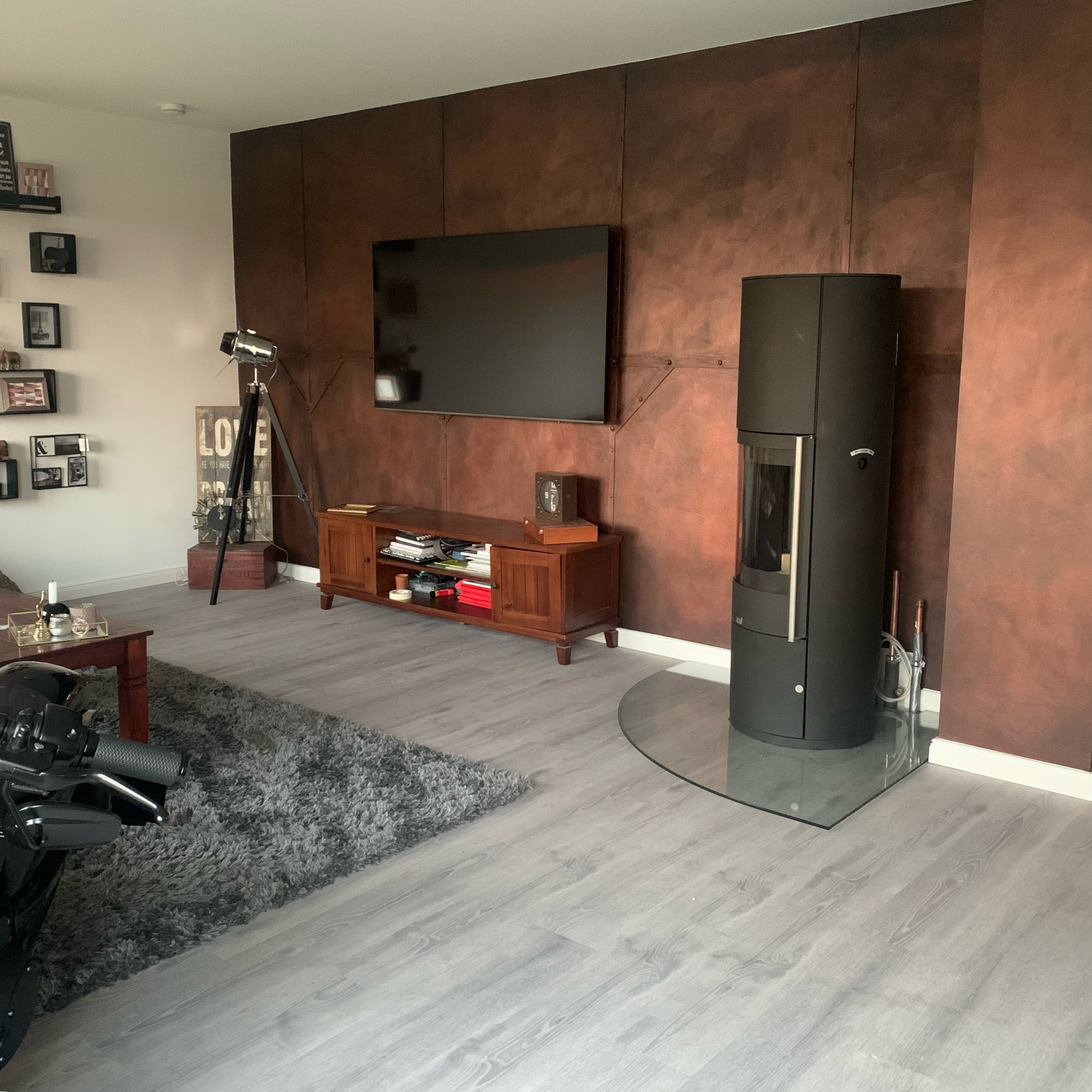 Wohnzimmer mit kupferbrauner Metallwand, Kaminofen und Wandmontiertem Fernseher
