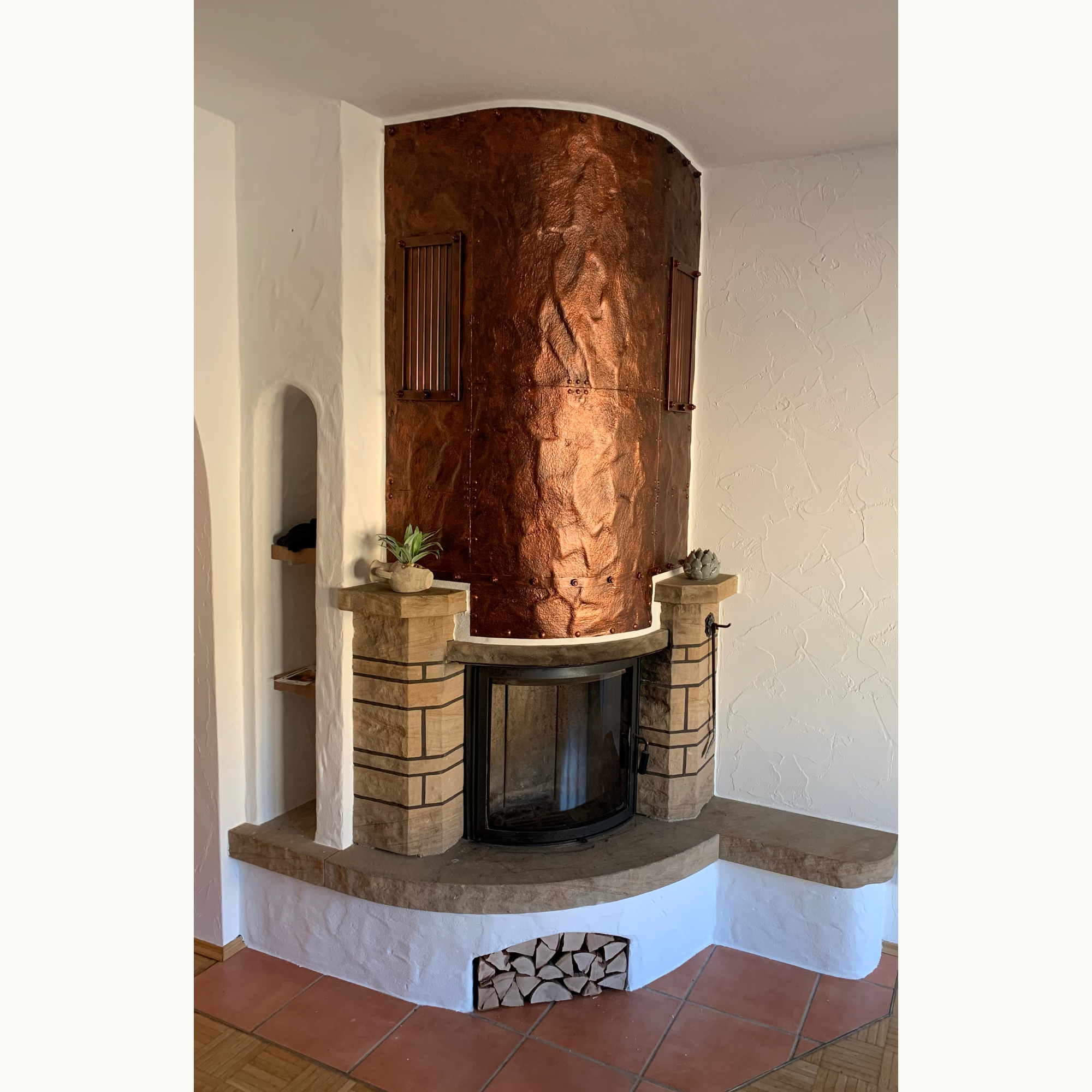 Kaminecke mit gewölbter Kupferverkleidung über einem Kamin und hellem Natursteinsockel