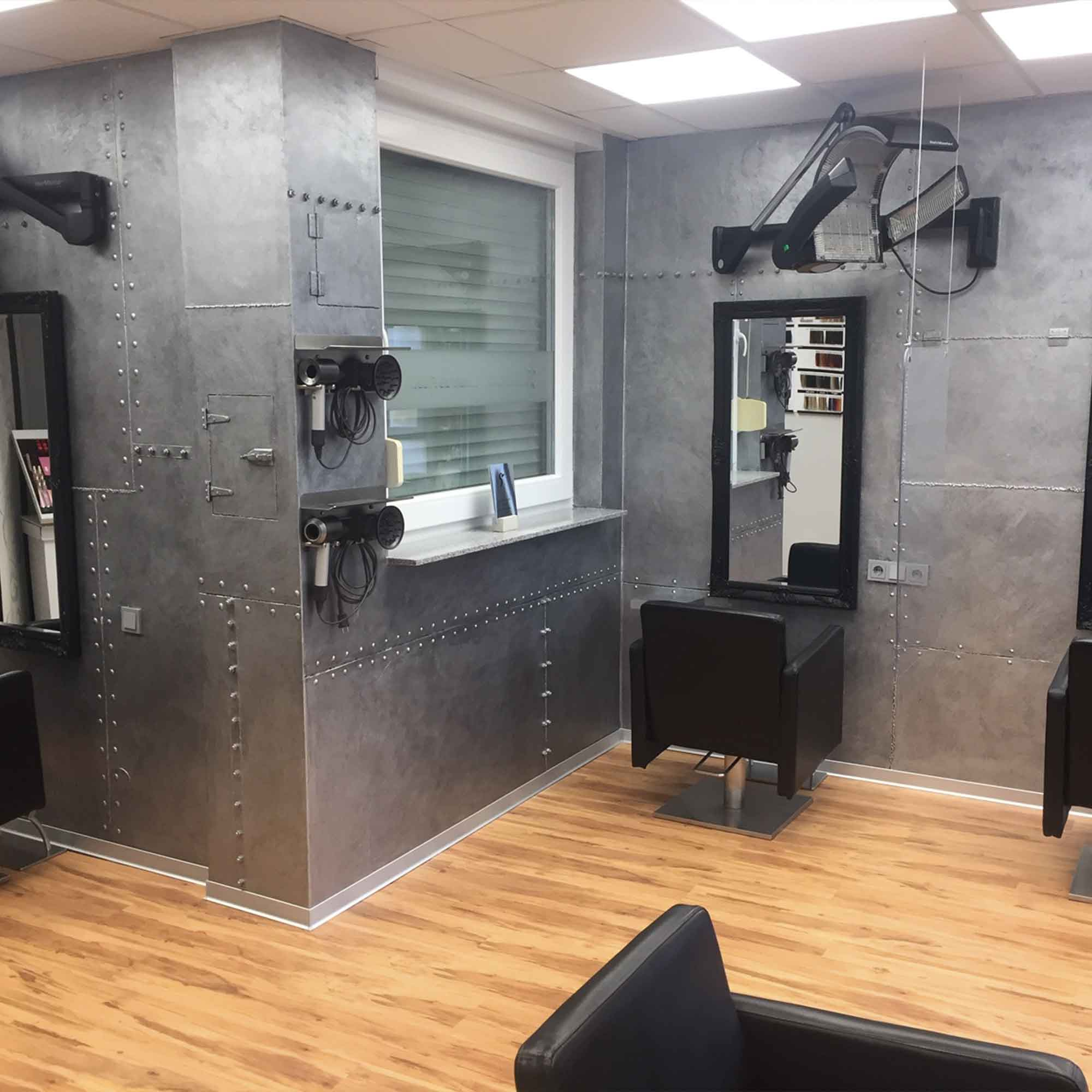 Friseursalon mit grauen, genieteten Metallwänden im Industrie-Look, Spiegeln und schwarzen Stühlen